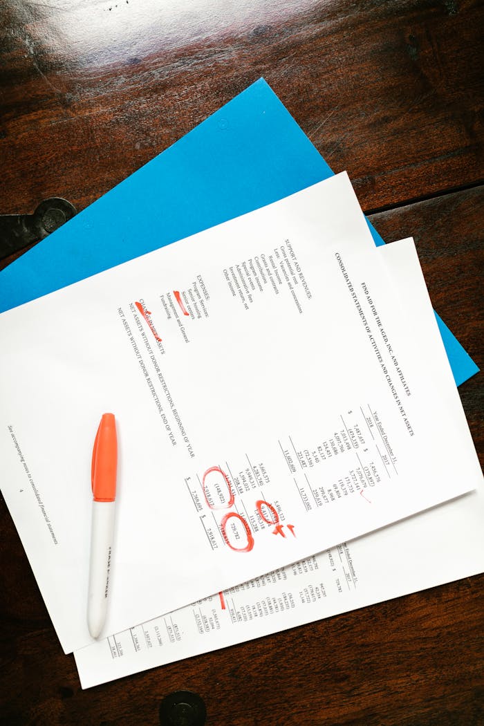 Overhead view of financial documents with red highlighted sections on a wooden desk.